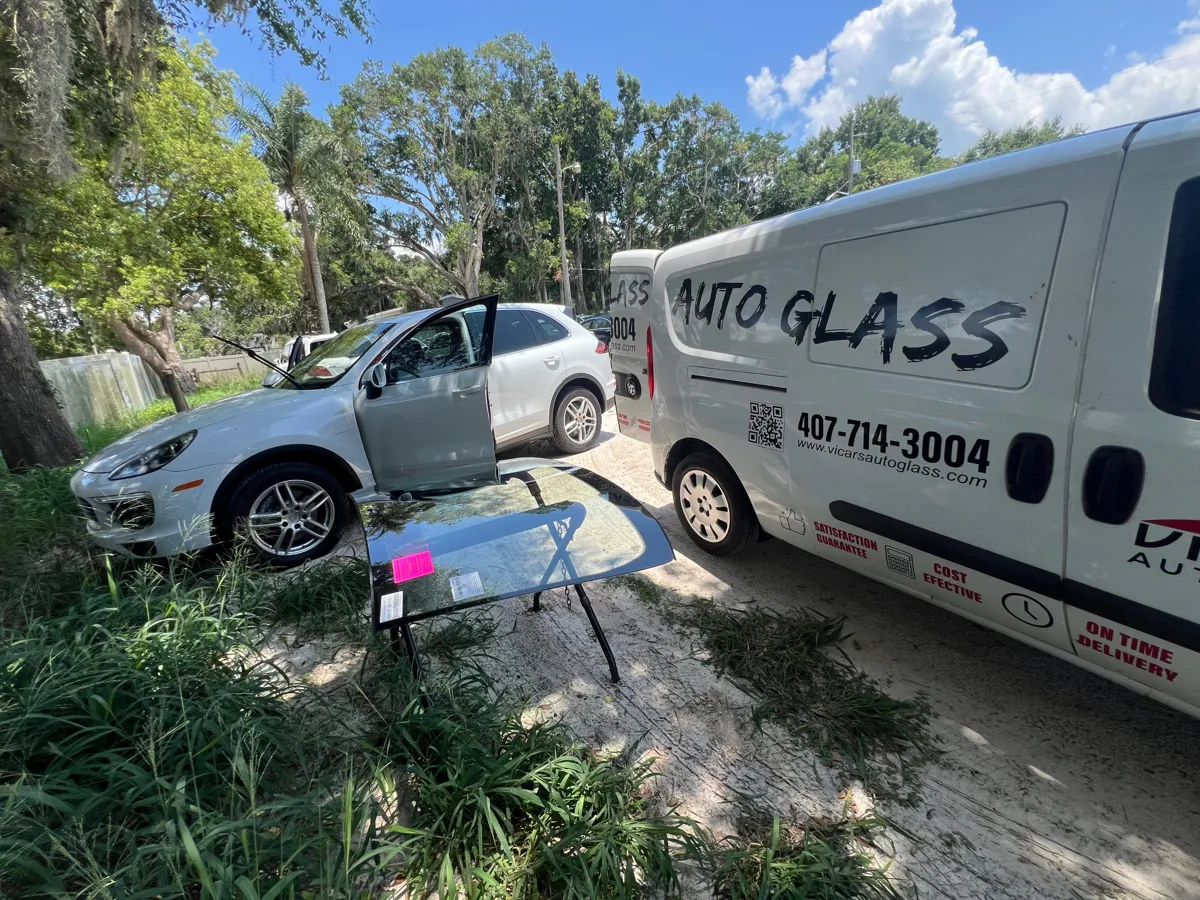 New windshield on a stand next to a Porsche Cayenne and the ViCars AutoGlass van in St. Cloud, FL